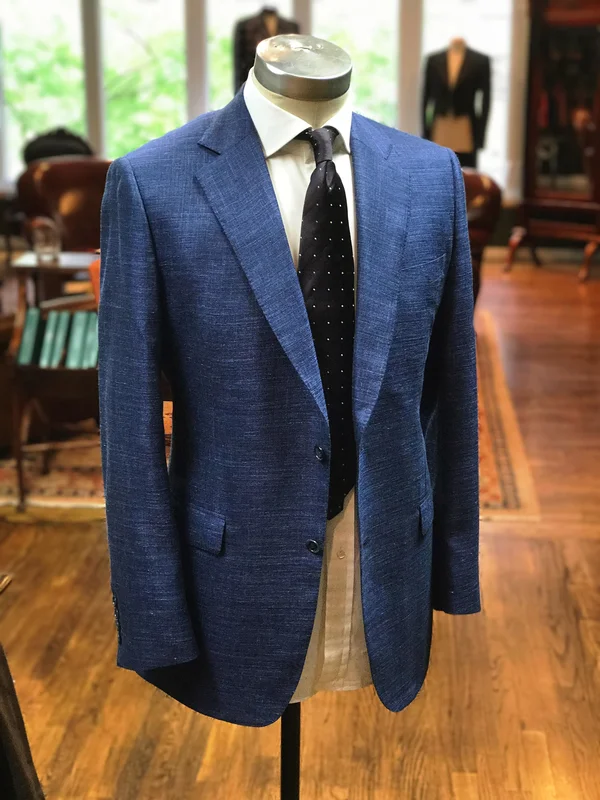 A navy jacket on a stand with a tie and pocket square, cloth samples behind.