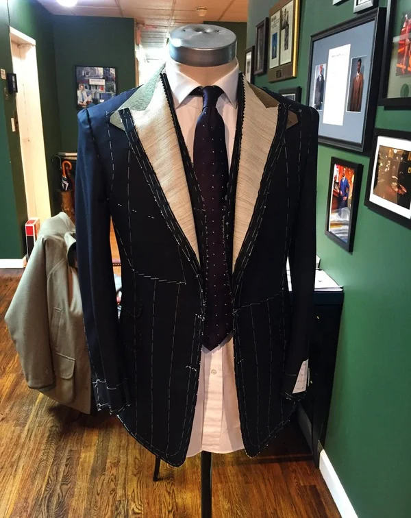 A dark windowpane suit on a stand, framed pictures on the wall behind.