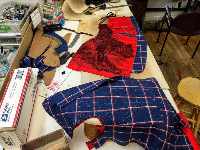 Cut cloth pieces in navy and red laid out on the workbench beside lining and a box of trimmings.