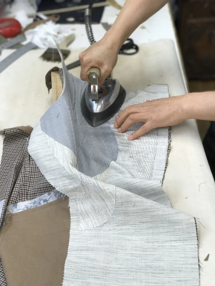 Two hands working an iron over a damp cloth on the pressing table.